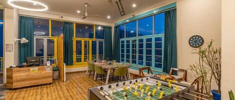 A room with a foosball table, a dartboard, and a table tennis table.