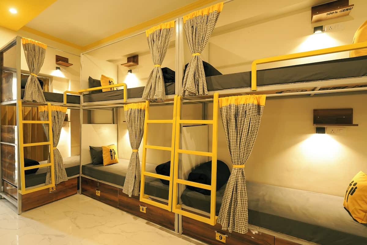 A dormitory room with bunk beds, checkered curtains, and a small shelf with a lamp.