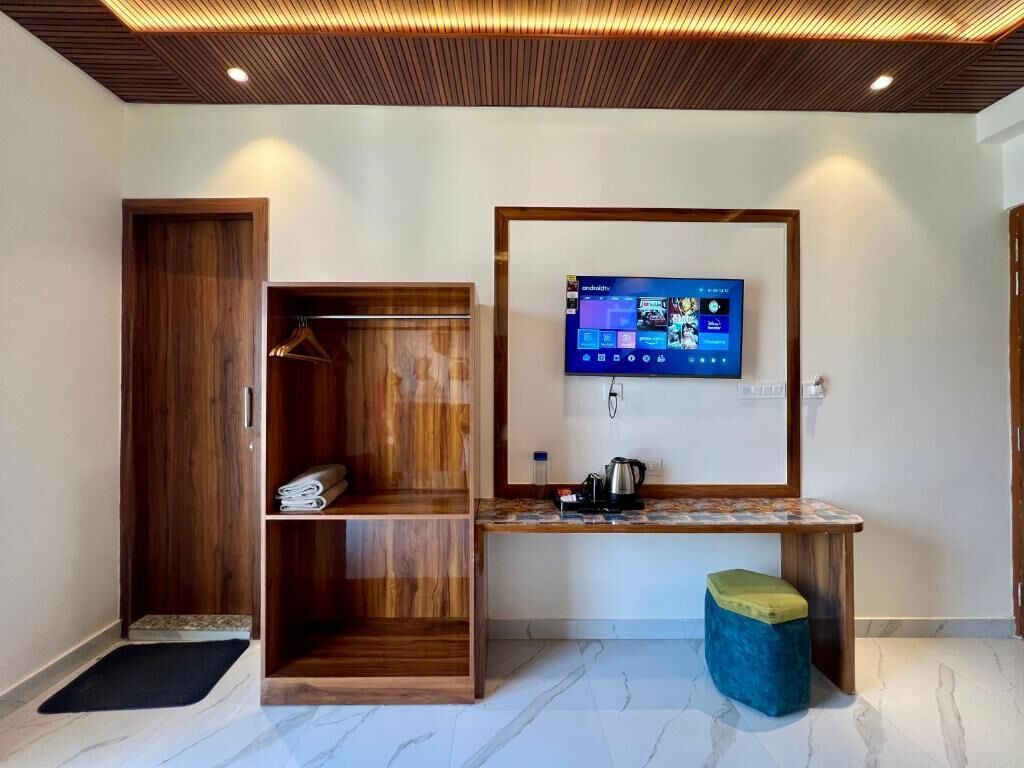 Ein modernes Zimmer mit einem Holzschrank, einem flachbildfernseher an der Wand, einem kleinen Tisch mit Wasserkocher und einer Bank.