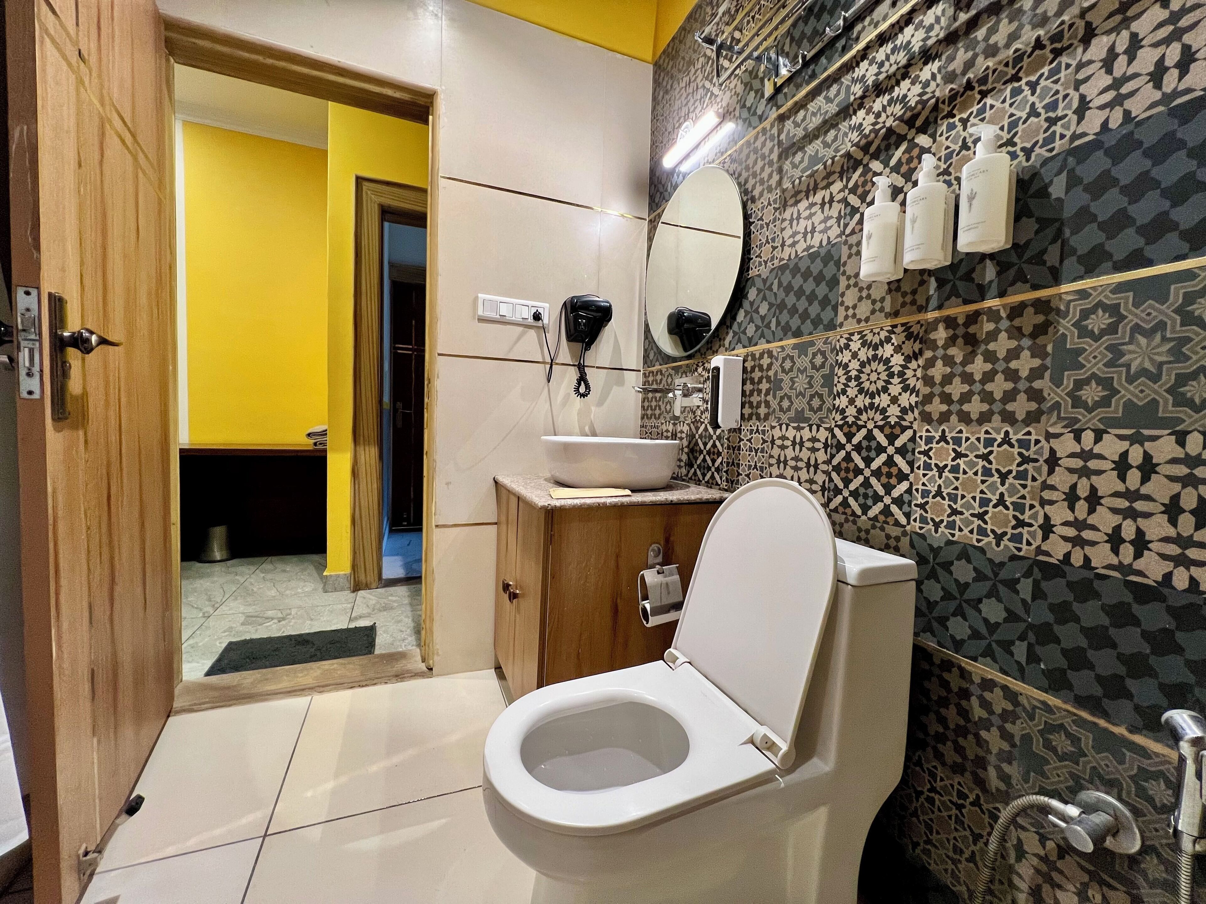 Een badkamer met toilet, wastafel en spiegel. Toiletartikelen zijn aan de muur bevestigd en er is een douchehoek.