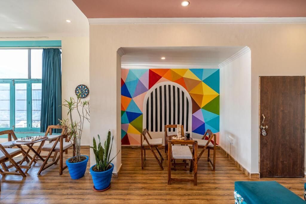 Een kamer met een houten vloer, een dartbord, kleurrijke geometrische wanddecoratie, een deur en een raam met gordijnen.