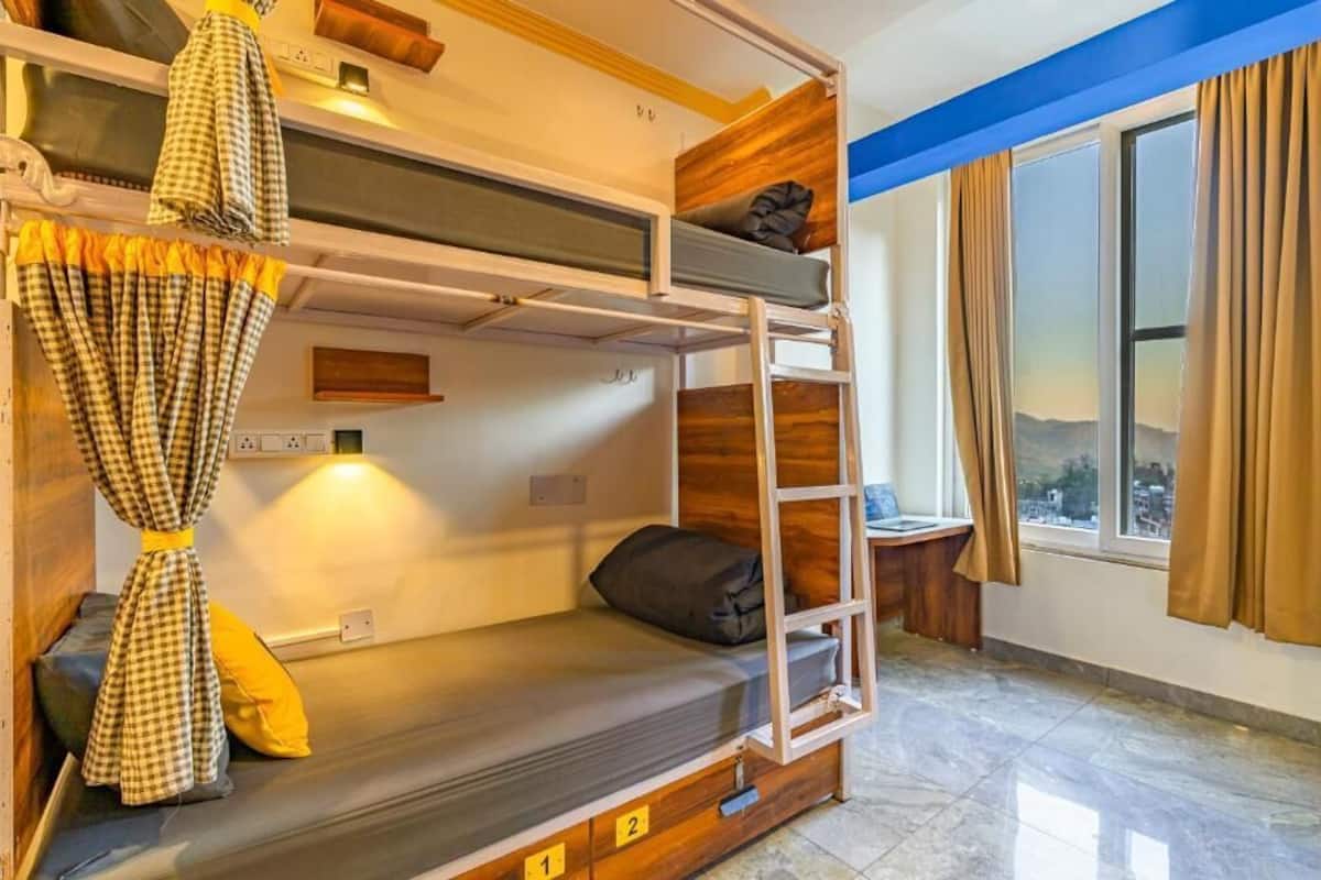 A bunk bed room with a ladder, a small table, and a window with curtains.