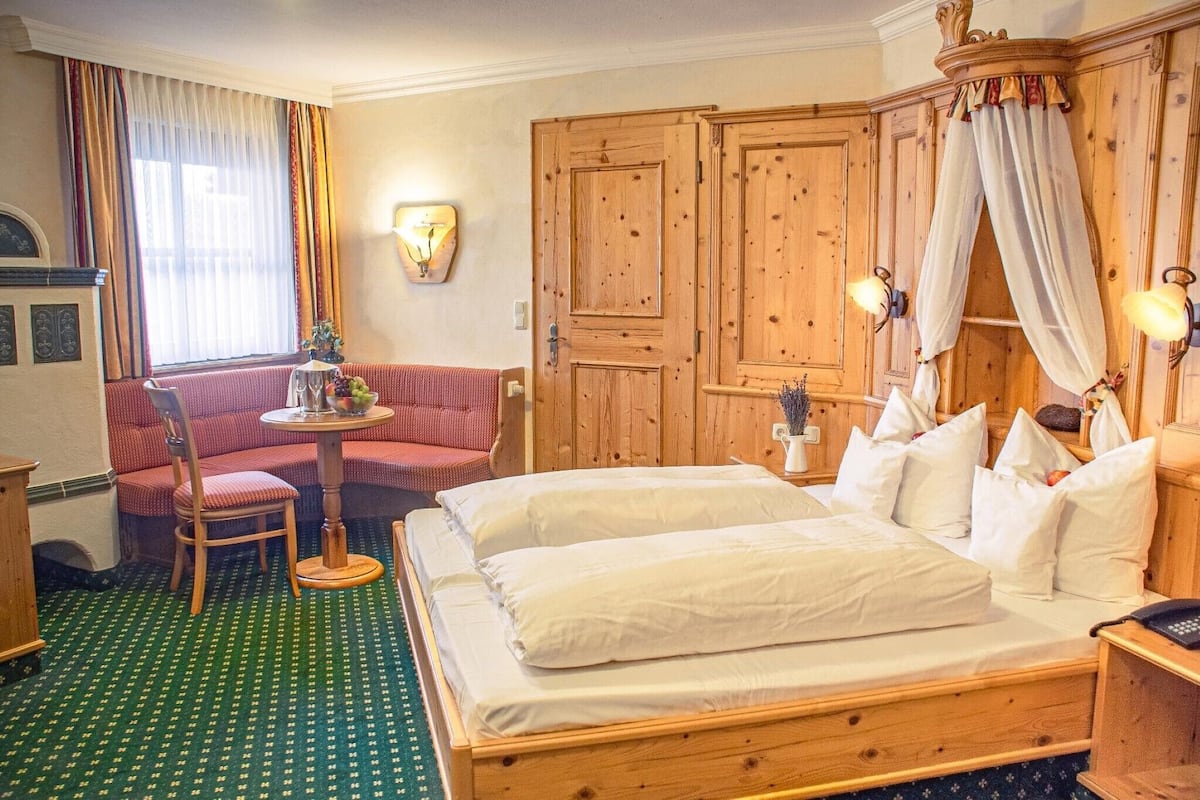 Et hotelværelse med en stor seng, et træskab, et lille bord med en vase, en rød sofa og et grønt tæppe med et mønster.