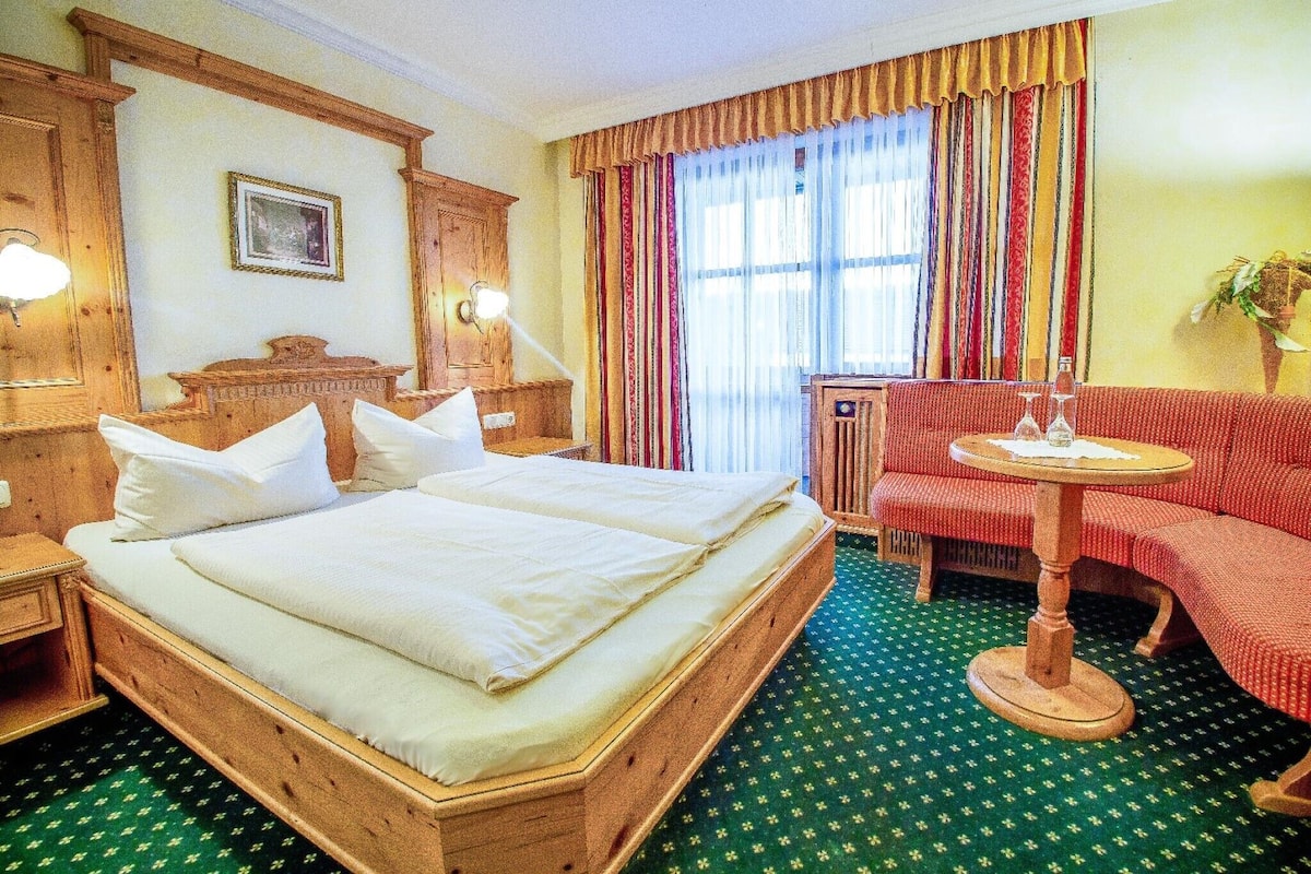 Et hotelværelse med en stor seng, et lille bord, en sofa og et vindue med gardiner.