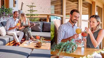 Un espacio moderno al aire libre con sillones y mesa, rodeado de plantas en macetas y una terraza de madera.