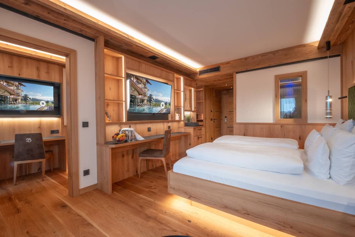Et moderne hotelværelse med trævægge, en stor seng, et skrivebord med stol og et fjernsyn, der viser et naturskønt udsigt.