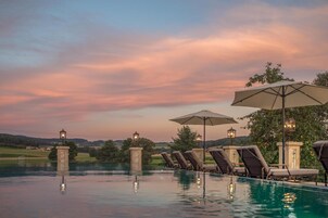 Zona junto a la piscina con sillones de descanso y sombrillas, rodeada de árboles y vistas al campo.