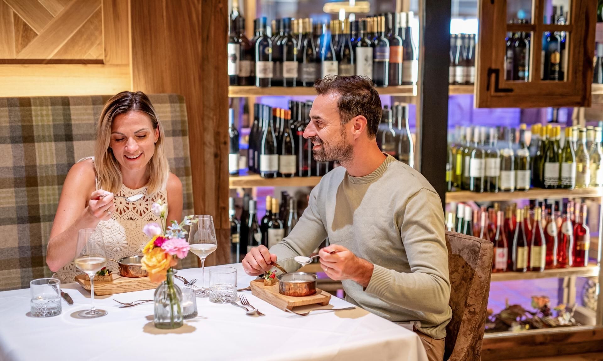 A couple dining at a table with a wine rack in the background.