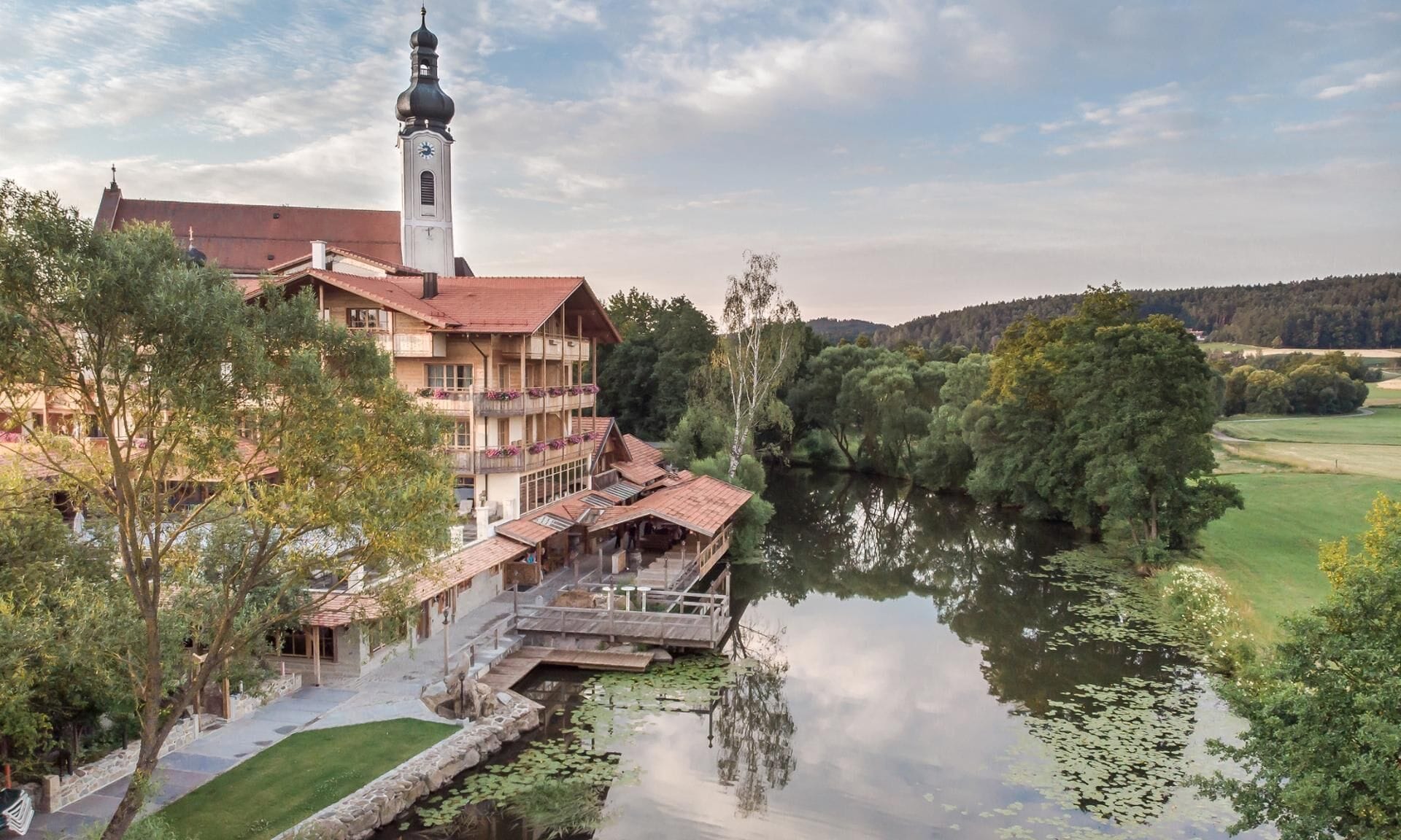Un edificio histórico con una torre de reloj, rodeado por un río y abundante vegetación.