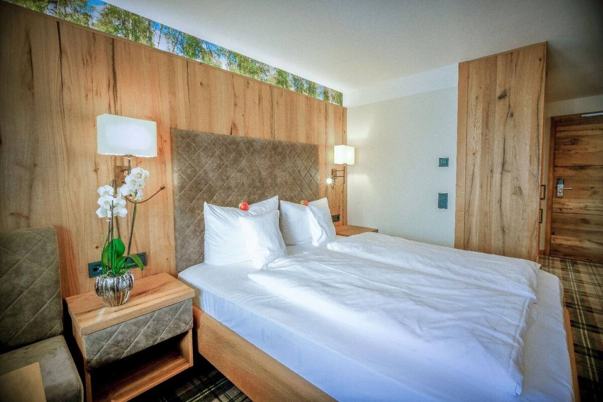 Et hotelværelse med sengegavl i træ, seng med hvide sengetøj, et natbord med en vase blomster og en træskab.