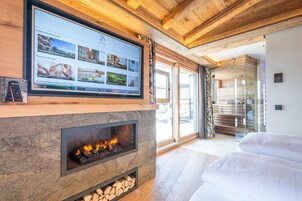 Una habitación de hotel moderna con chimenea de piedra, una pantalla grande mostrando información del hotel y vistas al área exterior.