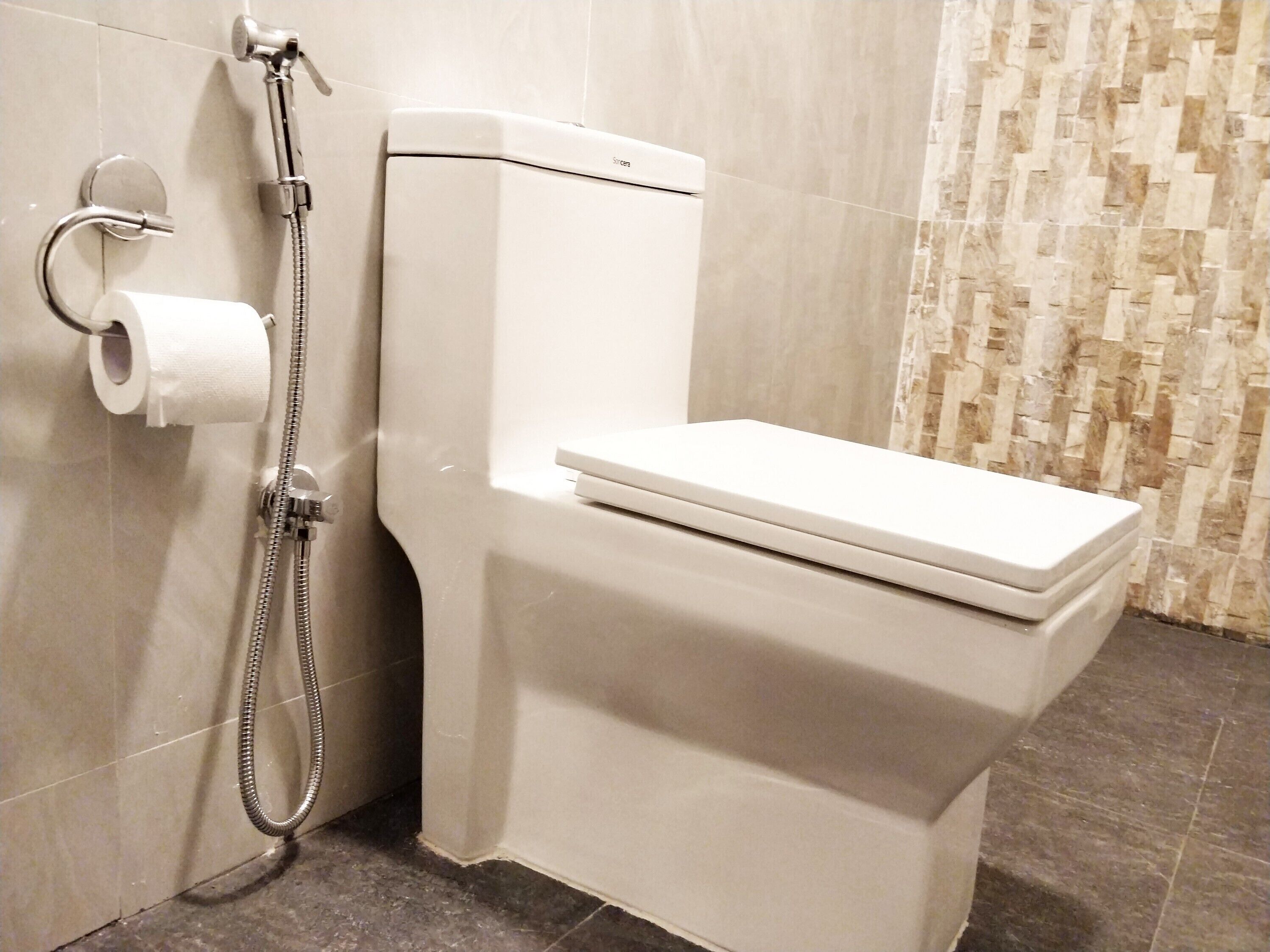 A modern bathroom with a white toilet, a shower head, and a toilet paper holder.
