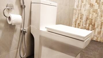 A modern bathroom with a white toilet, a shower head, and a toilet paper holder.