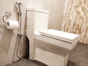 A modern bathroom with a white toilet, a shower head, and a toilet paper holder. - Quays Himalayan Hotel & Apartments  (Kathmandu)