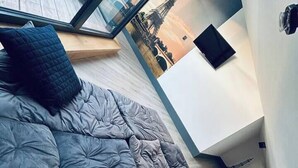 Quarto moderno com uma cama grande, vista para a paisagem urbana através de uma janela ampla e uma pequena área de trabalho.