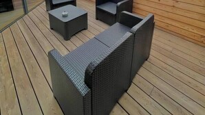 Um terraço no topo com móveis de vime e piso de madeira.