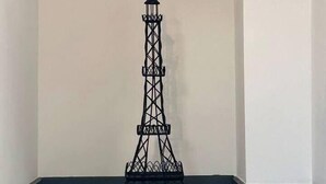 Um quarto com piso de madeira, paredes brancas e uma escultura da Torre Eiffel em metal preto.