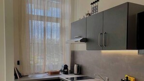 A modern kitchen with dark cabinets, a built-in oven, a sink, and a dining area with a table and chair. - Studio Anna near Mulhouse (Wittelsheim)