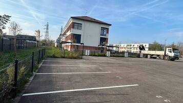 A parking lot with a building in the background, a fence, and a clear sky.