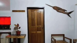A room with a wooden door, a red-lit television, a potted plant, a wooden bench, and a wall-mounted fish decoration. - CASETTA HOMESTAY (General Luna)