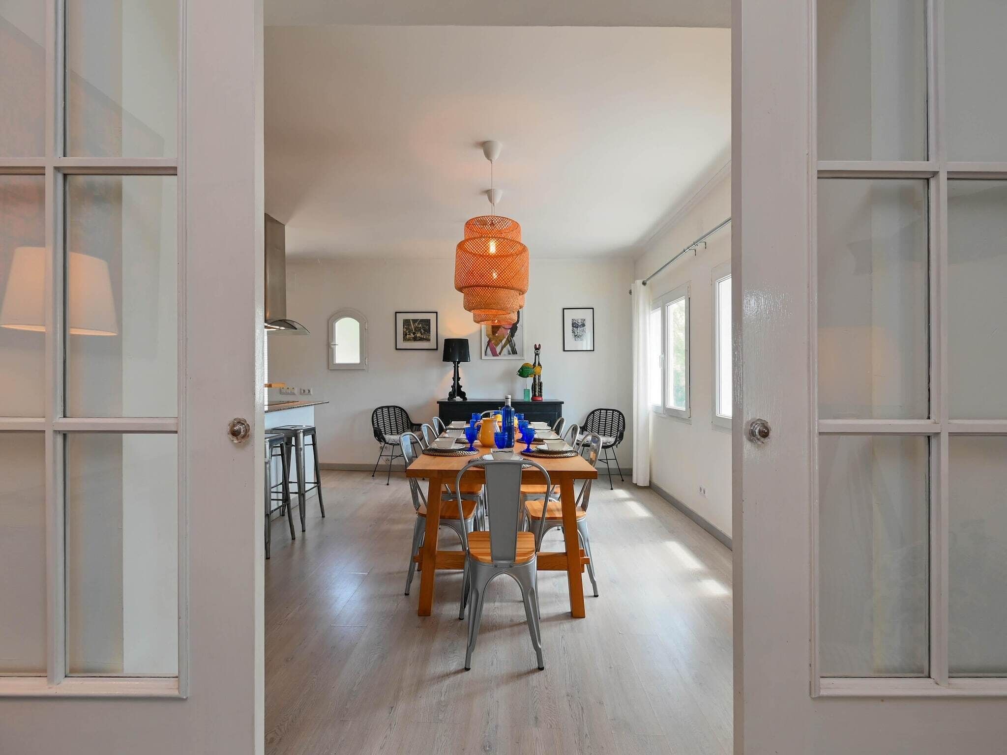 An open-plan living and dining area with a large wooden table, chairs, and a hanging orange light fixture.