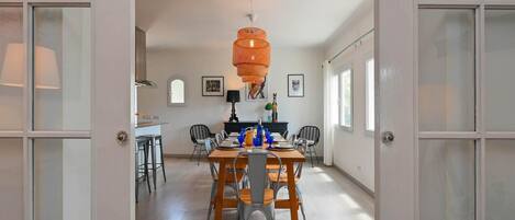 An open-plan living and dining area with a large wooden table, chairs, and a hanging orange light fixture.