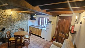 Una cocina rústica con paredes de piedra, vigas de madera, una mesa de comedor con sillas, un microondas y un refrigerador.