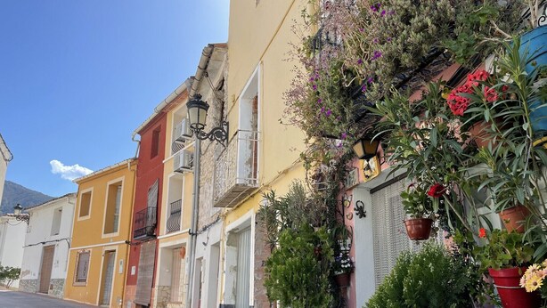 Una calle adoquinada bordeada de edificios coloridos, algunos con balcones y plantas colgantes.