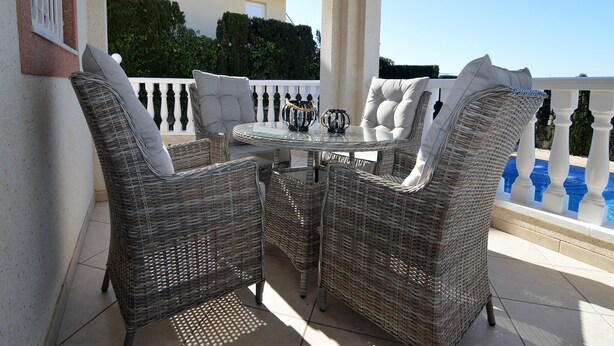 A patio with wicker furniture, a glass table, and a view of a building and pool.