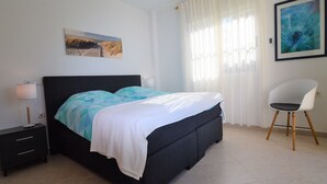 A bedroom with a bed, a chair, a nightstand, and two paintings on the wall.