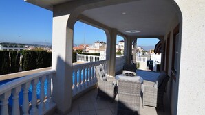 A balcony with wicker furniture, a view of the sea, and a cityscape in the background.