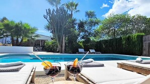 Un área junto a la piscina con sillones de descanso y dos copas de vino tinto sobre una mesa de madera.