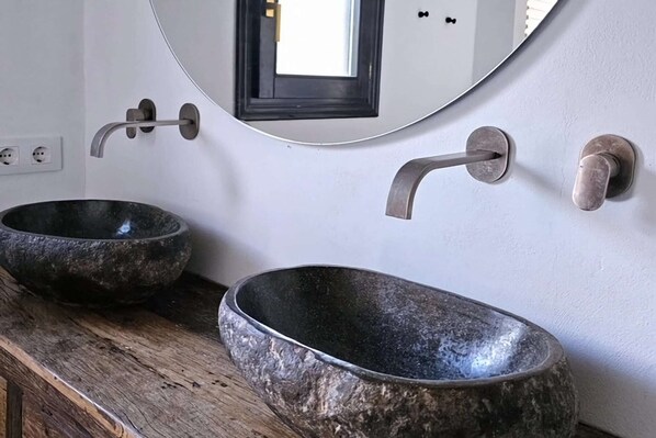 Two stone sinks with modern faucets mounted on a white wall.