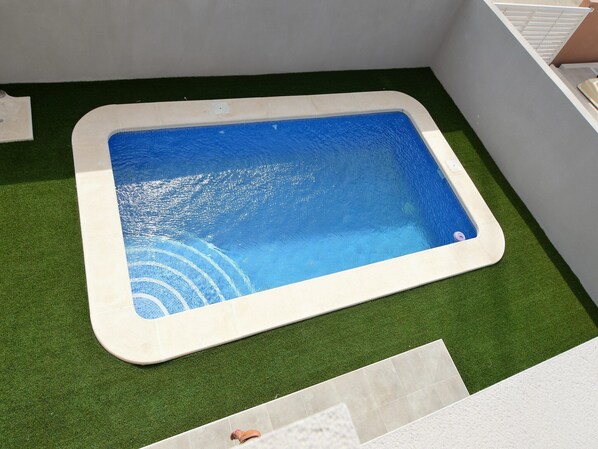 A rectangular pool with a white border, surrounded by artificial green grass.