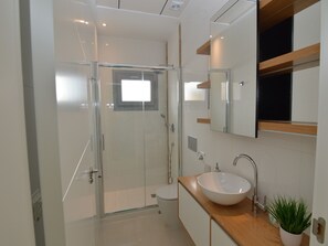 Casa de banho moderna com cabine de chuveiro em vidro, lavatório branco e espelho sobre a bancada.