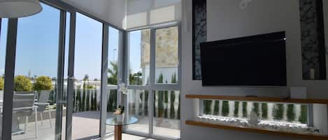 Relax in this stylish living room with a large flat-screen TV, floor-to-ceiling glass doors opening to a balcony with a view.