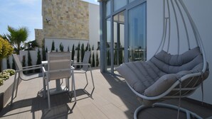Un patio exterior moderno con una silla colgante, dos sillas blancas y un muro de piedra.
