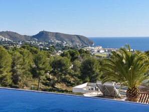 Una piscina amb vistes a una població costanera, un turó amb edificis i una palmera.