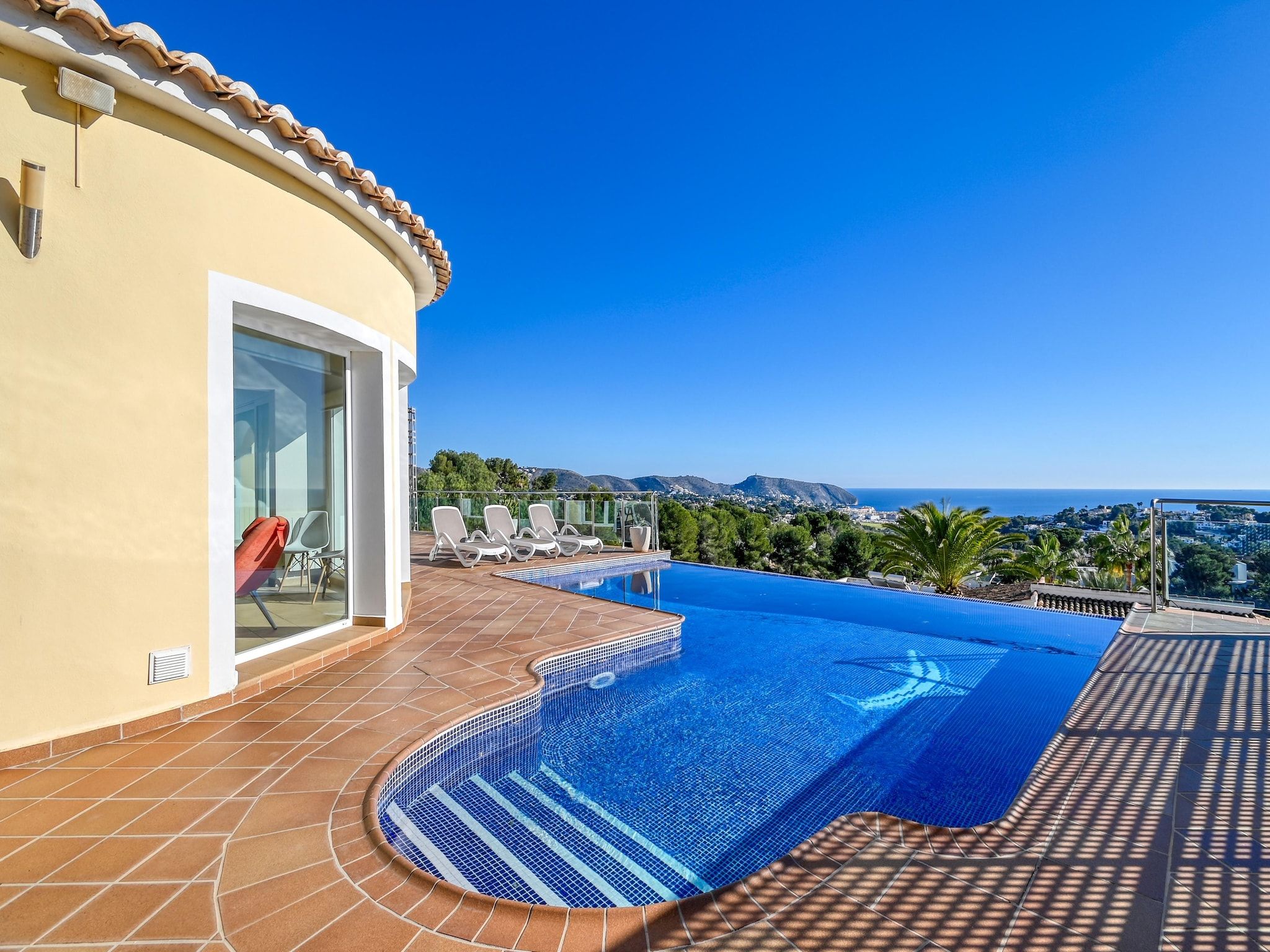 A swimming pool with a clear view of the ocean and hills in the background.