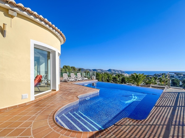 A swimming pool with a clear view of the ocean and hills in the background.