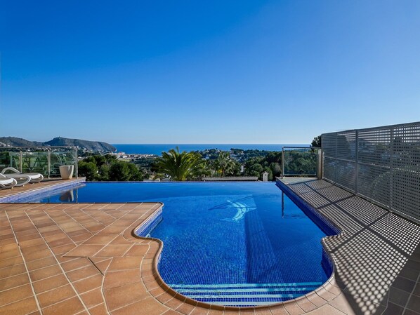 A swimming pool with a clear view of the sea and a hilly landscape in the background.