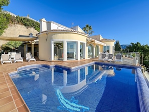 A poolside area with a clear blue pool, white lounge chairs, and a building with large windows and a curved roof.