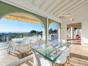 A spacious outdoor dining area with a glass table and white chairs, overlooking a scenic view.