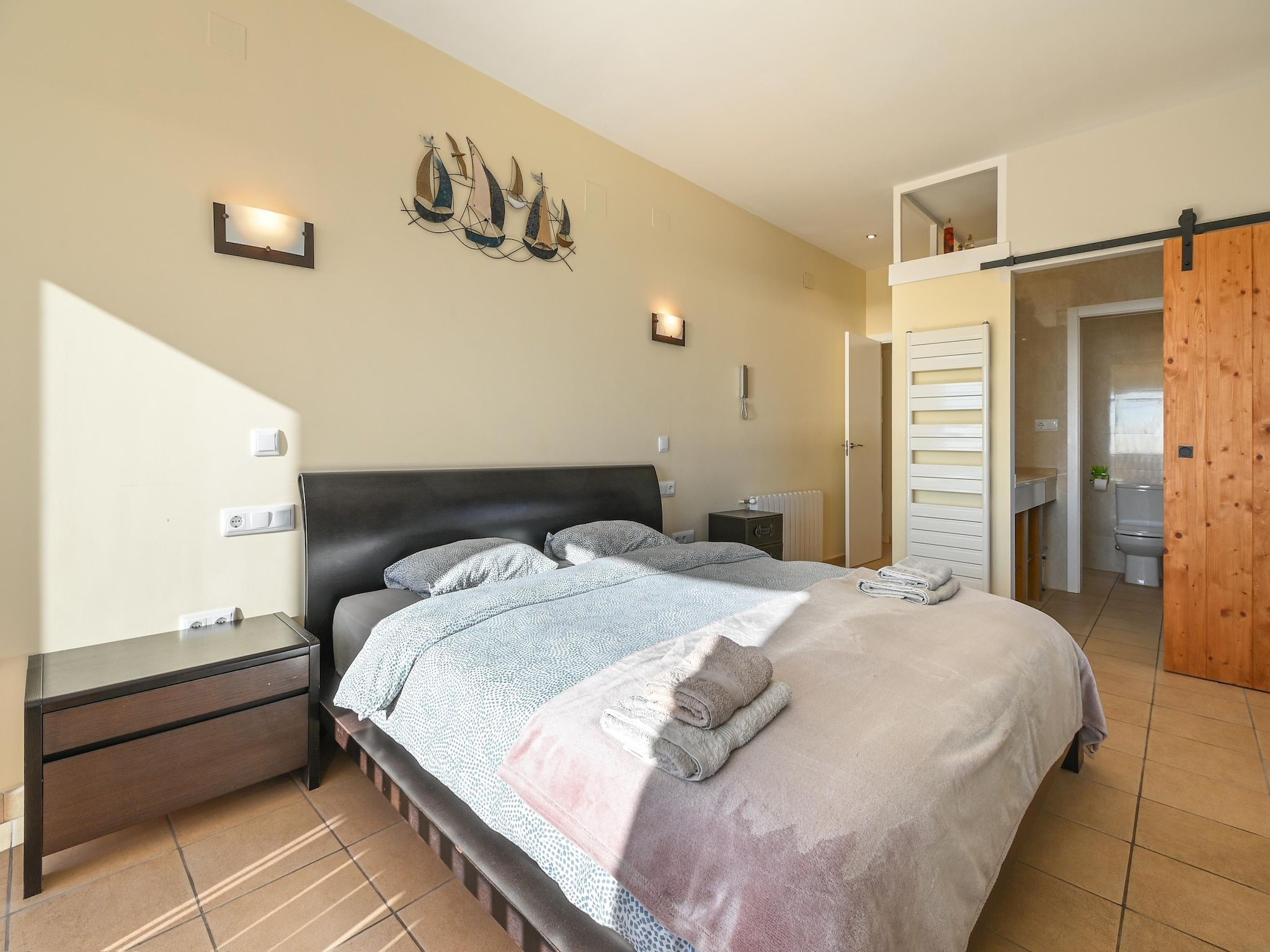 A bedroom with a bed, bedside tables, a wall-mounted light, and a wooden door.