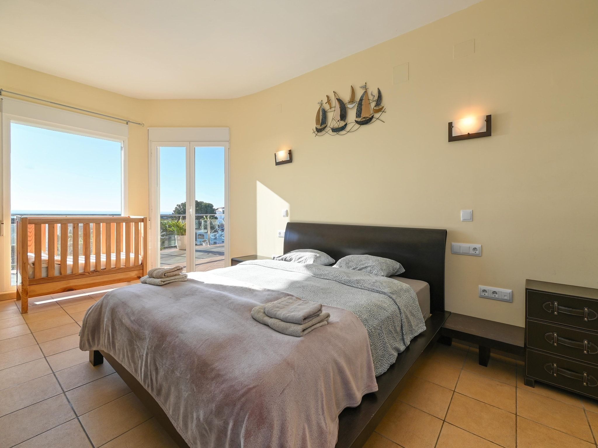 A bedroom with a bed, a nightstand, a dresser, and a balcony with a wooden railing.
