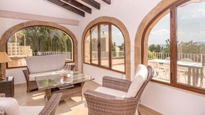 A sunlit patio with wicker furniture, large arched windows, and a view of the surrounding landscape. - Villa near Montgó with Pool and Beach (Javea)