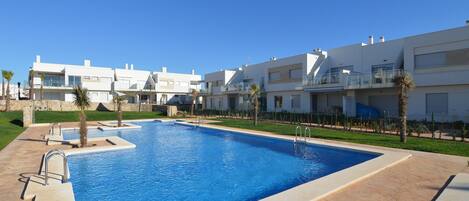 A modern hotel with a swimming pool, multiple balconies, and a clear blue sky.