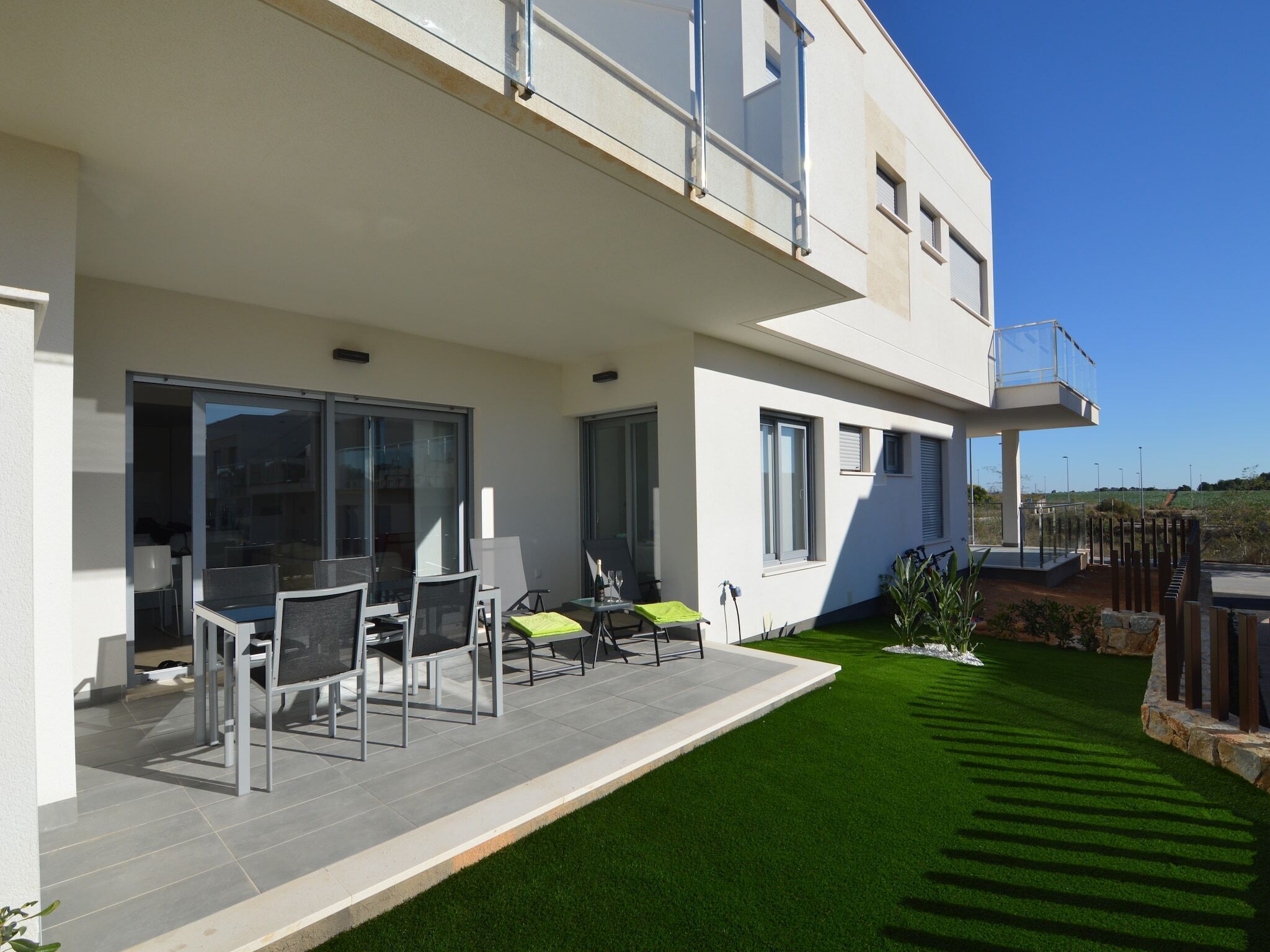 A modern two-story house with a patio area featuring outdoor furniture and a well-maintained lawn.