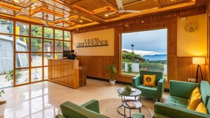 A reception area with a wooden ceiling, green sofas, a reception desk, and a large window with a view of the landscape.