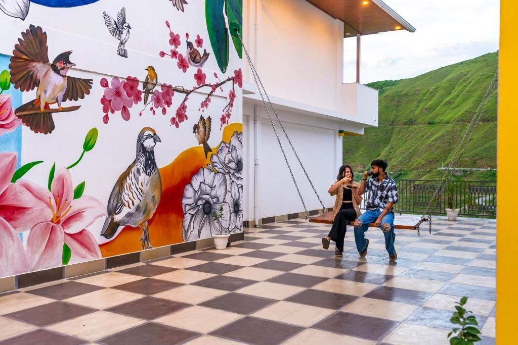 Un sol à carreaux, une fresque représentant des oiseaux et des fleurs, et un bâtiment avec une colline verdoyante en arrière-plan.